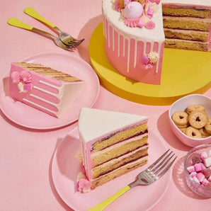 Pretty In Pink Cake with raspberry ripple sponge, vanilla buttercream, white chocolate drip, and pink decorations on a yellow stand.